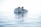A ferry with a white body and colorful stripes sails on a calm, expansive ocean with clear skies. The vessel has multiple decks and appears to be carrying numerous passengers. The water is a light blue, reflecting the bright sunlight that creates a serene and peaceful atmosphere.
