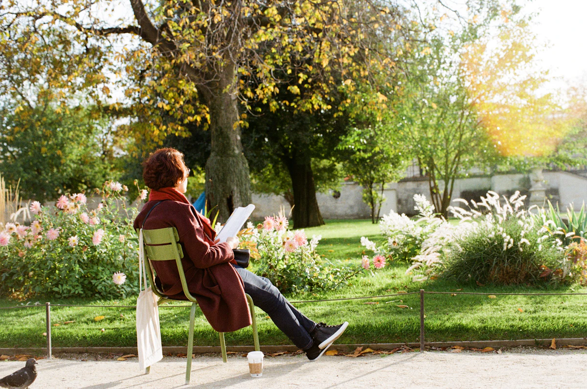 Person sitting outdoors reading a book among flowers