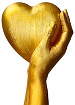 A golden hand holding a heart-shaped object, with a smooth, textured surface. The hand appears to be sculpted or painted gold, giving a sense of luxury and elegance.