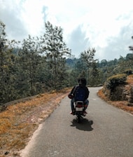 A biker girl riding along a winding mountain road with lush greenery and blue skies in the background.