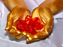 Close-up of a hand gently holding a polished rose quartz against a deep purple background with soft gold highlights.
