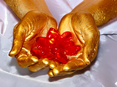 Close-up of a hand gently holding a polished rose quartz against a deep purple background with soft gold highlights.