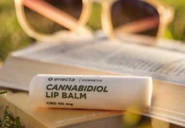 Cannabidiol lip balm on book on grass during daytime