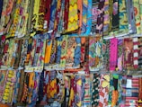 A display of various colorful, patterned fabrics arranged neatly in rows. The fabrics showcase an array of intricate designs, vibrant colors, and textures, creating a visually stimulating scene.