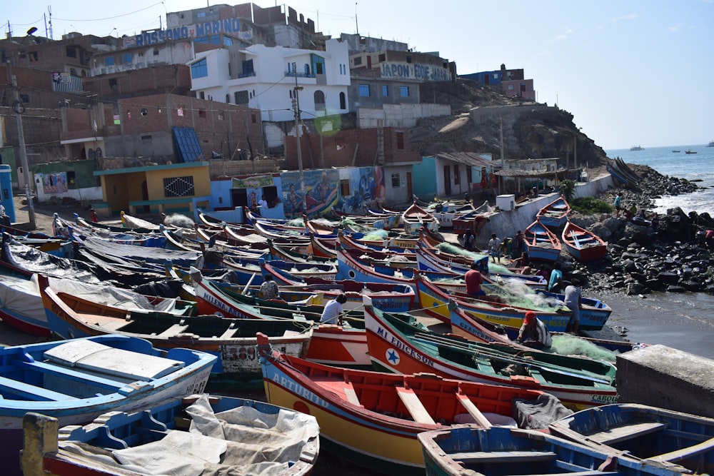 multicolored dinghy boats near seashore beside buildings viewing body of water under blue and white sky during daytime