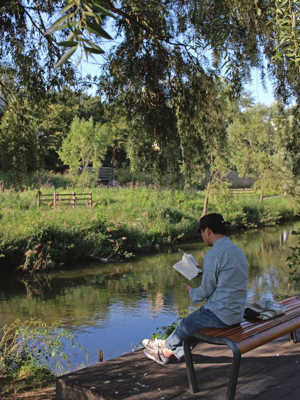 man reading book while sitting near body of water