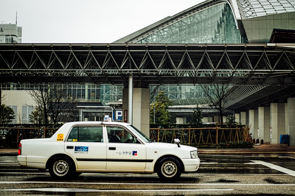 A sleek white taxi from Taksi Al Abbas waiting outside a modern office building in Kuwait.