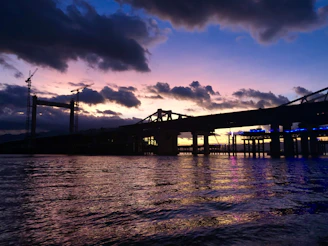 A panoramic view of a modern bridge construction site at sunset, showcasing cranes and workers.
