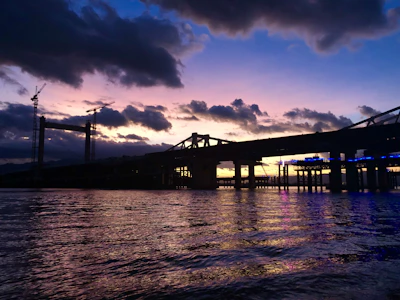 Construction crew working on a sturdy bridge over a river at sunset.