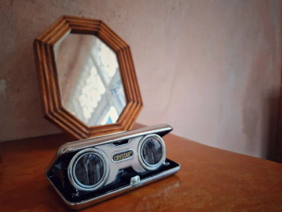 A cozy corner featuring a vintage mirror above a wooden table with a glass display case showcasing delicate keepsakes.