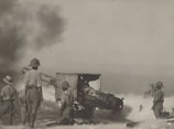 Several soldiers in uniforms and pith helmets operate and stand around a large piece of artillery. Smoke and dust fill the air, suggesting recent firing. The environment is sparse, and visibility is somewhat obscured by the smoke.