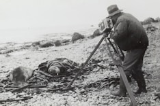 grayscale photography of man taking photo near seashore