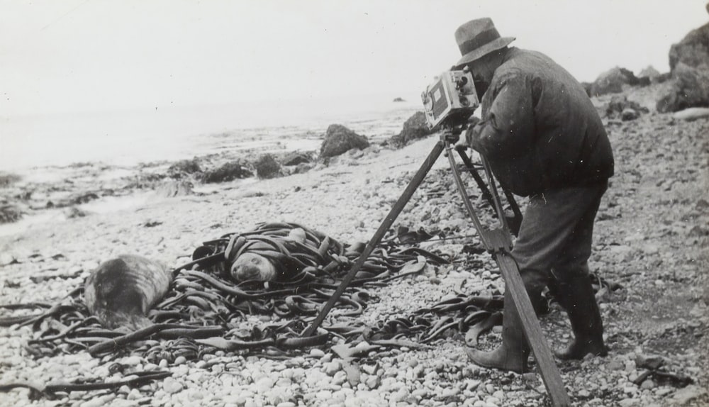Fotografía en escala de grises de un hombre tomando una foto cerca de la orilla del mar