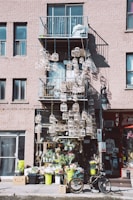 A storefront adorned with numerous decorative birdcages hanging from a balcony, with a collection of potted plants and flowers displayed below. A bicycle is parked in front of the shop, adding to the eclectic and artistic vibe.