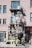 A storefront adorned with numerous decorative birdcages hanging from a balcony, with a collection of potted plants and flowers displayed below. A bicycle is parked in front of the shop, adding to the eclectic and artistic vibe.