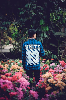 A joyful person wearing a vibrant 'Faith Over Fear' shirt, standing in a sunlit garden with blooming flowers.