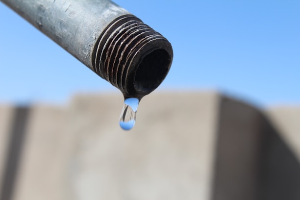 A close-up photo of a plumber fixing a pipe with water droplets, showing hands working with tools.