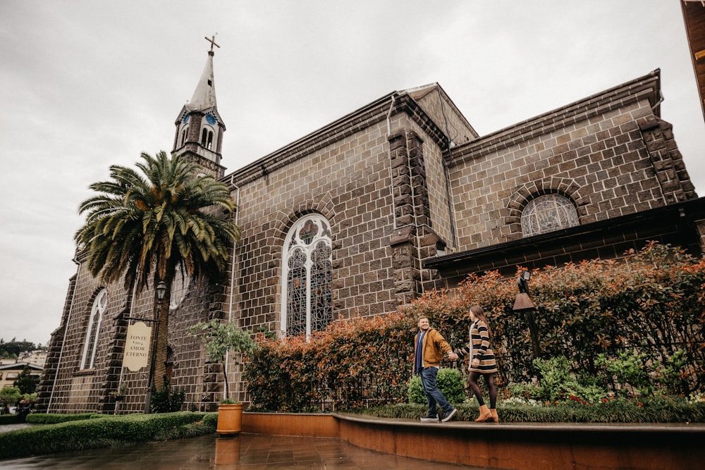 man and woman walking in front of brown building