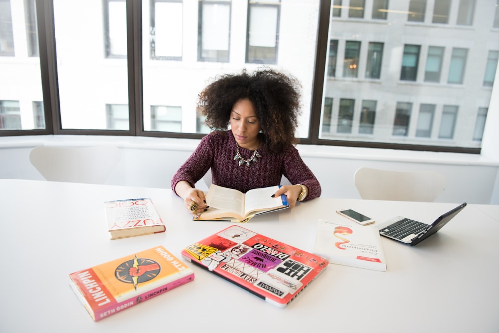 woman sitting beside table reading book