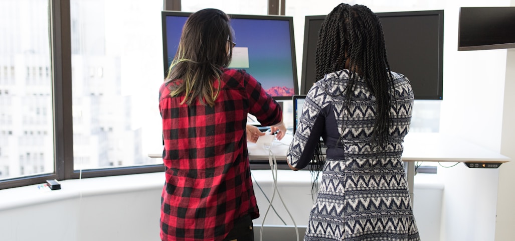 two women standing in front of two black monitors