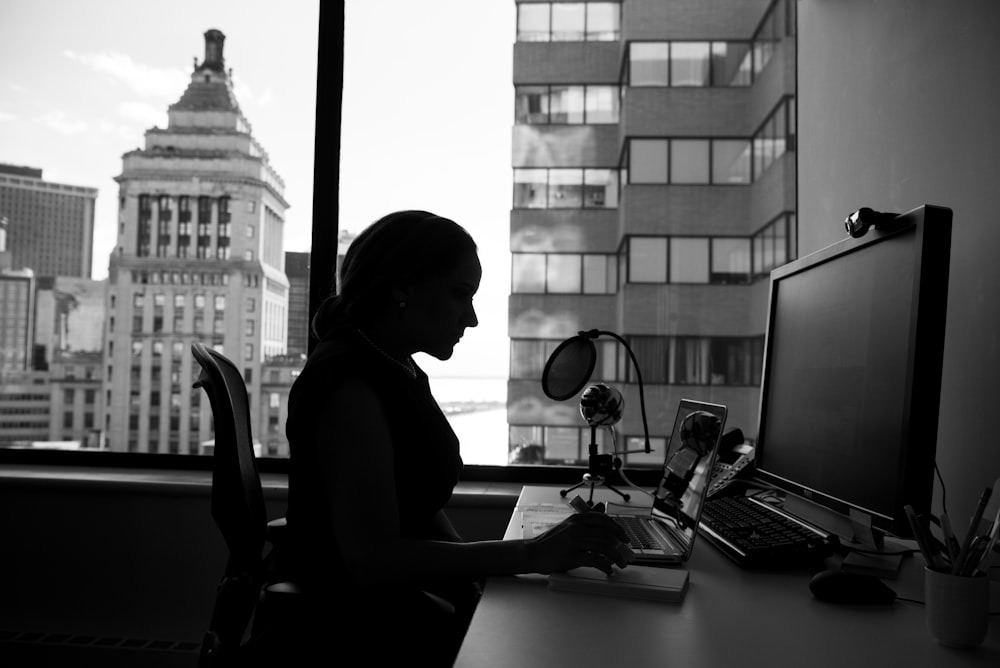 fotografia in scala di grigi di donna seduta davanti a un computer