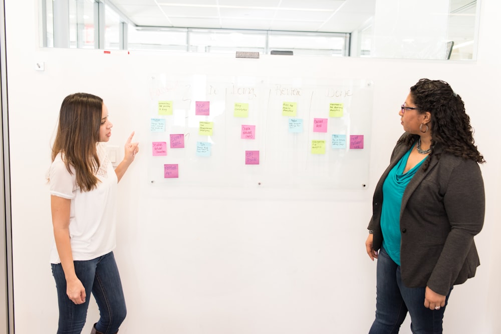 two women standing beside white board