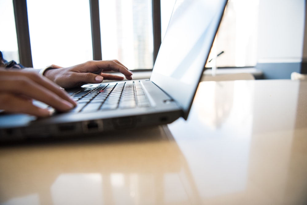 person using black laptop on brown table