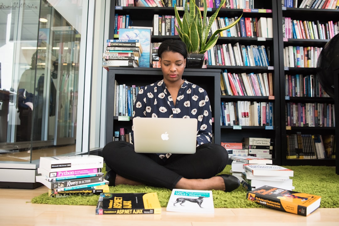 woman sitting down surrounded by books while using MacBook