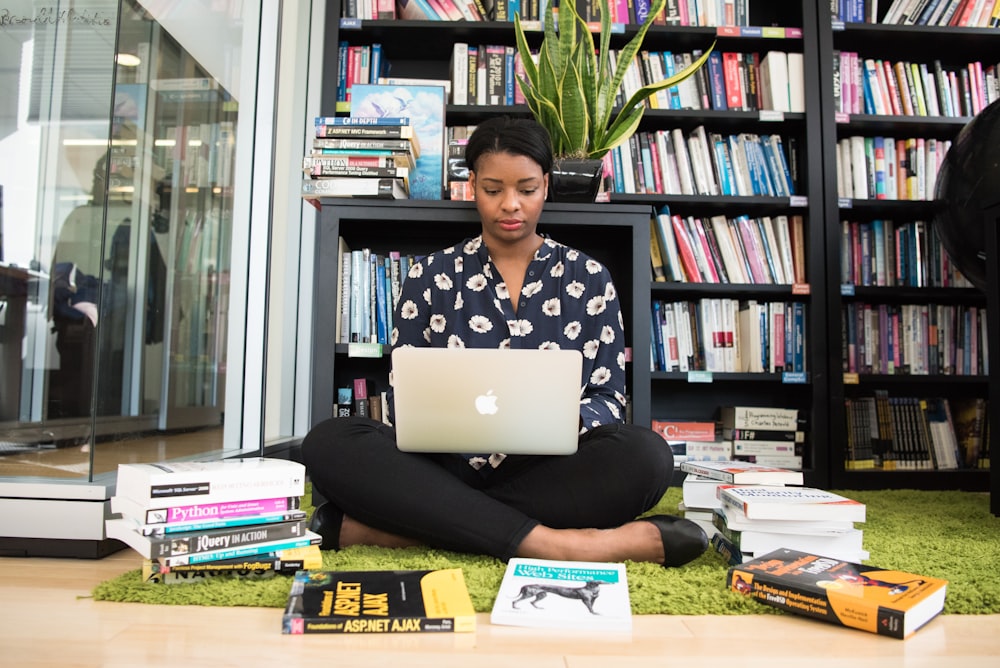 woman sitting down surrounded by books while using MacBook