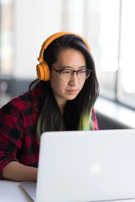 woman using MacBook and wearing yellow headphones
