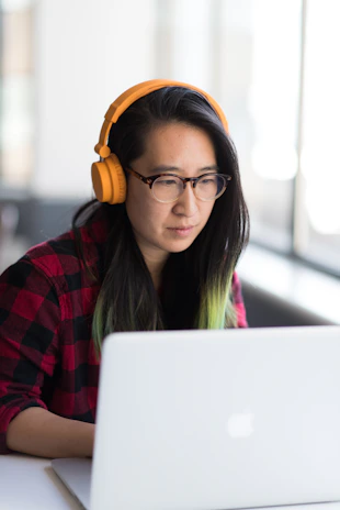 woman using MacBook and wearing yellow headphones