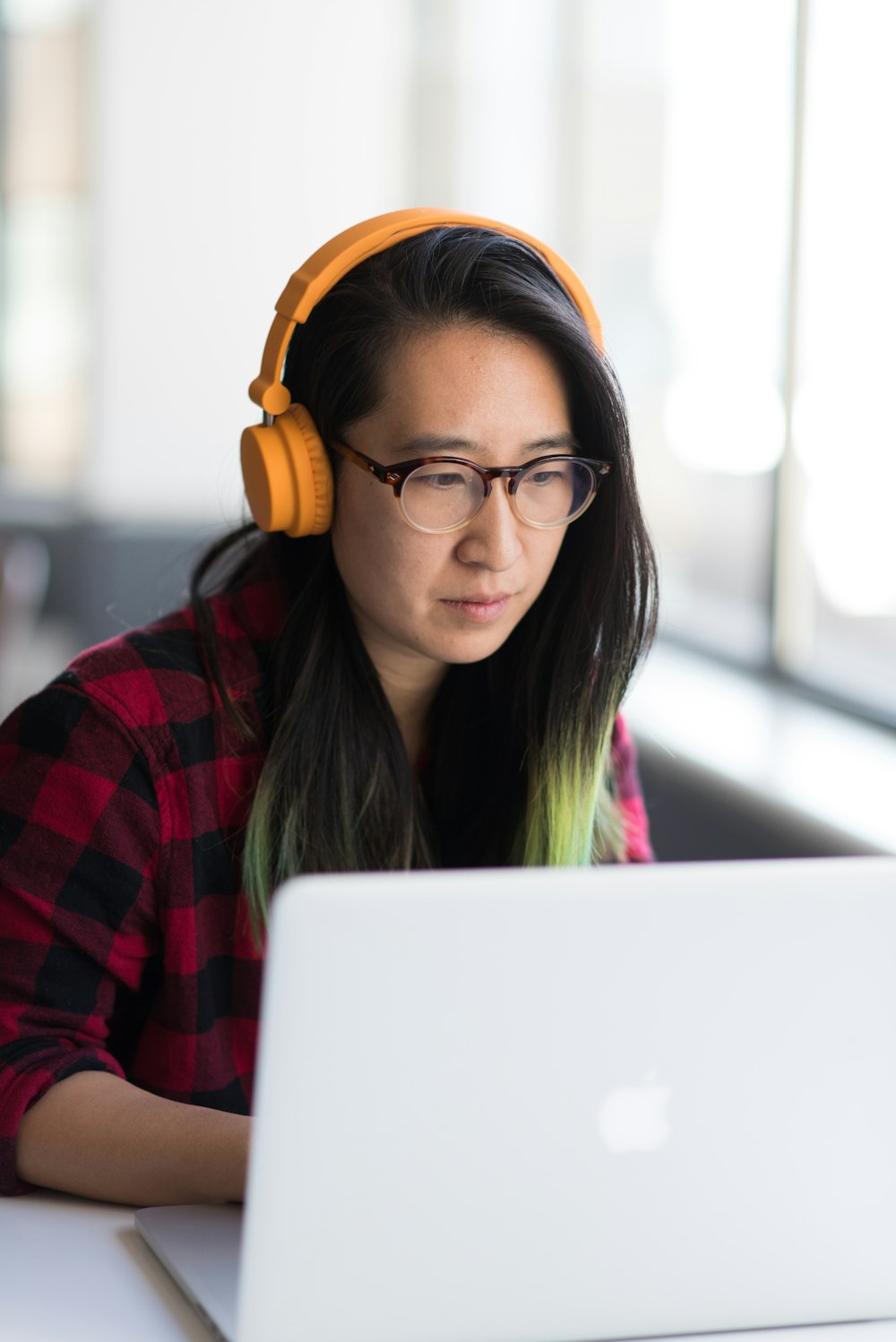 MacBookを使用し、黄色いヘッドフォンを装着した女性