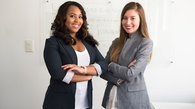 two women in suits standing beside wall