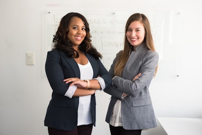 two women in suits standing beside wall successful teams background