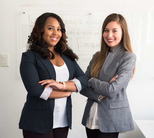 two women in suits standing beside wall