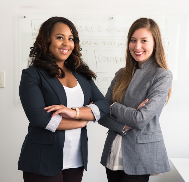 two women in suits standing beside wall