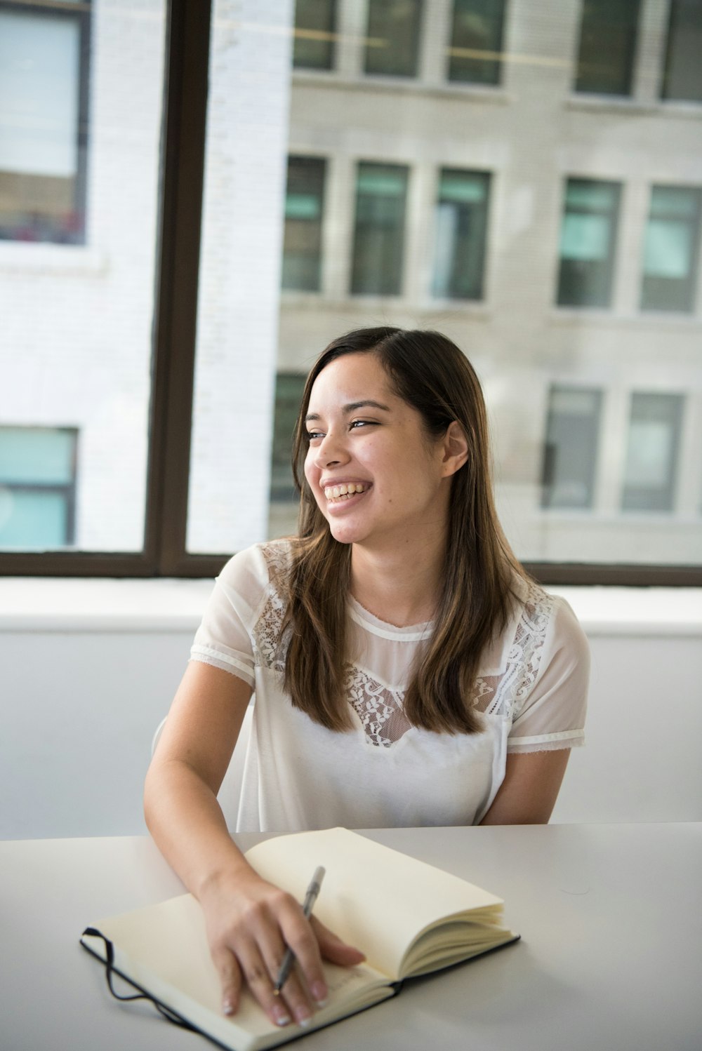 smiling woman sitting at the table with her hands on an open book