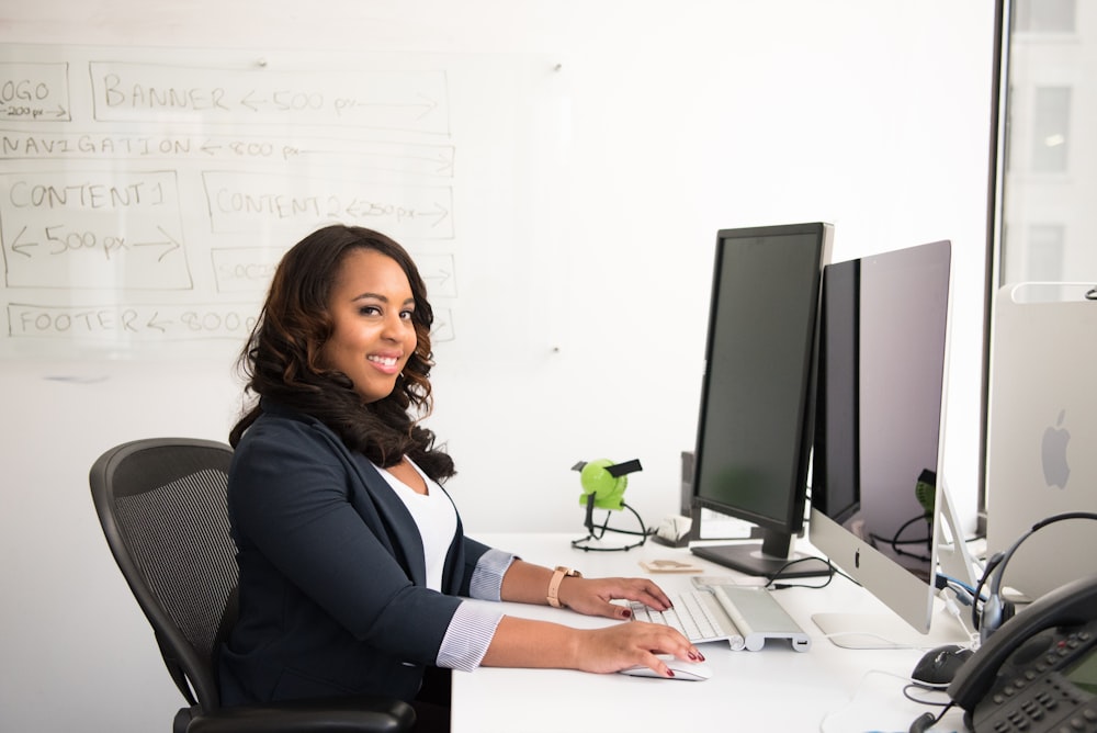 shallow focus photo of woman in black jacket using iMac