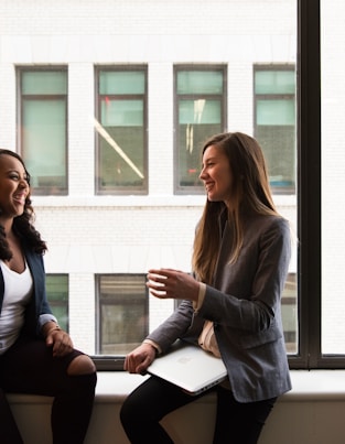 two woman sitting by the window laughing