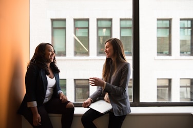 two female professionals sitting by a window and talking