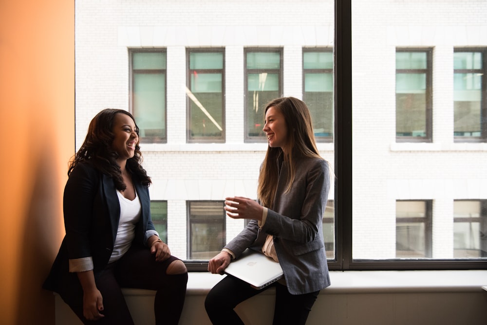 two woman sitting by the window laughing