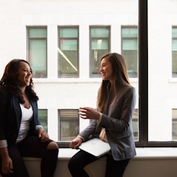 two woman sitting by the window laughing