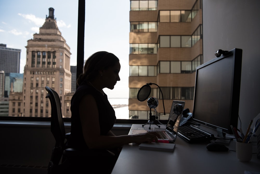 컴퓨터 모니터와 키보드를 맨 위에 놓고 책상 앞에 앉아 있는 여자