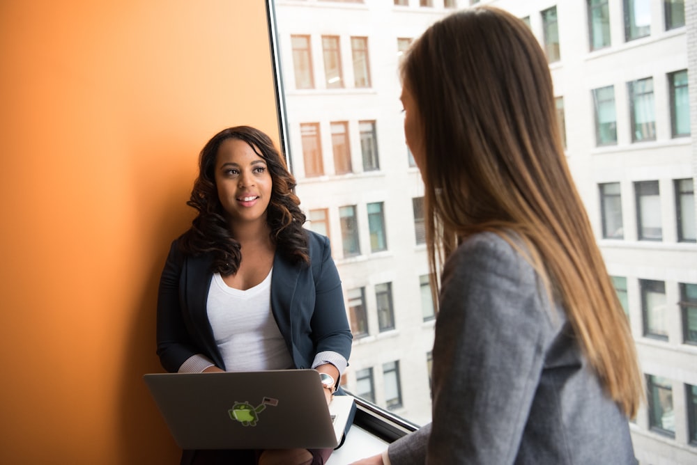 woman standing infront of woman holding laptop