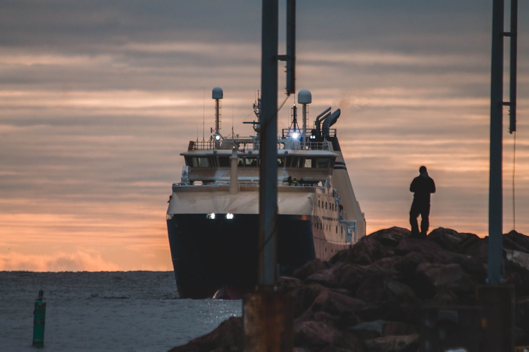 man standing on rocks overlooking ship on body of water