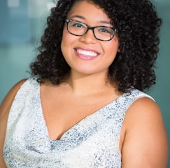 woman in brown-framed eyeglasses and white and gray cowl-neckline sleeveless top