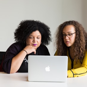 two women looking at the screen of a MacBook