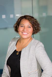 Portrait of a smiling young woman with curly hair in a casual office setting.