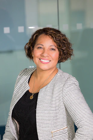 Portrait of a smiling young woman with curly hair in a casual office setting.