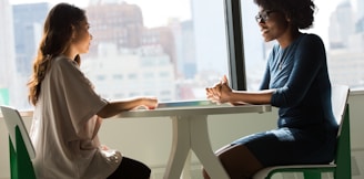 two women sitting beside table and talking